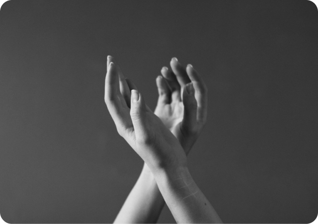 Zu sehen sind zwei sich überkreuzende Hände vor neutralem Hintergrund. Die Hände sind entspannt und äesthetisch angeordnet.